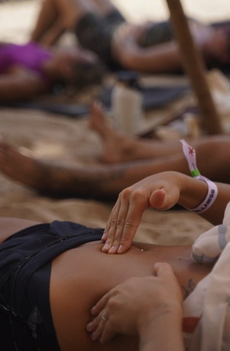 Mãos fazendo a autodrenagem no abdome, na praia